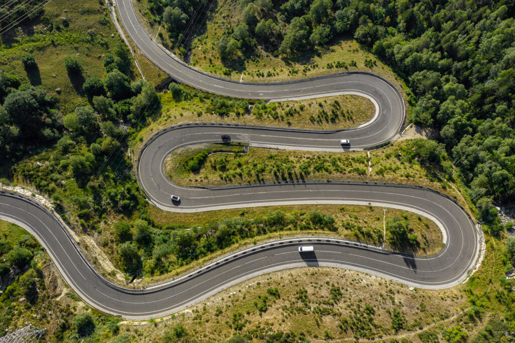 Luftaufnahme einer kurvenreichen Serpentinenstraße in den katalanischen Pyrenäen, umgeben von grünen Hängen und Bäumen.
